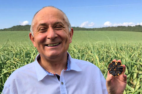 Daniel Gonzalez, Inhaber von Black Gonzalez, hält lächelnd eine aufgeschnittene Knolle schwarzen Knoblauchs in der Hand