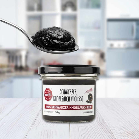 Ein Glas schwarzer Knoblauch Mousse mit einem Löffel Mousse